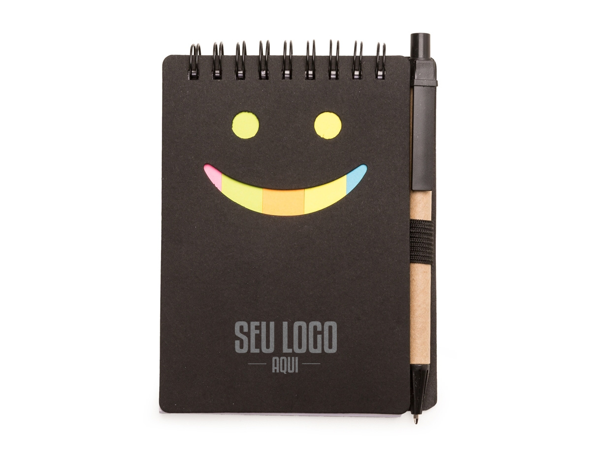Bloco de anotações ecológico com caneta de papelão. Possui detalhe "smile" na capa frontal(verso liso), caneta ecológica com acabamentos em plástico acionada por clique, primeira folha(branca) com cinco blocos autoadesivos coloridos com aproximadamente 20 folhas cada, bloco amarelo com aproximadamente 20 folhas e 70 folhas brancas pautadas.