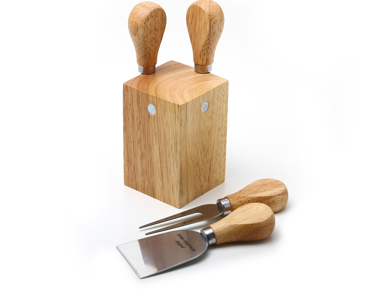 Kit queijo composto por faca reta, faca com ponta, espátula e garfo inox em uma base de madeira com ímãs.