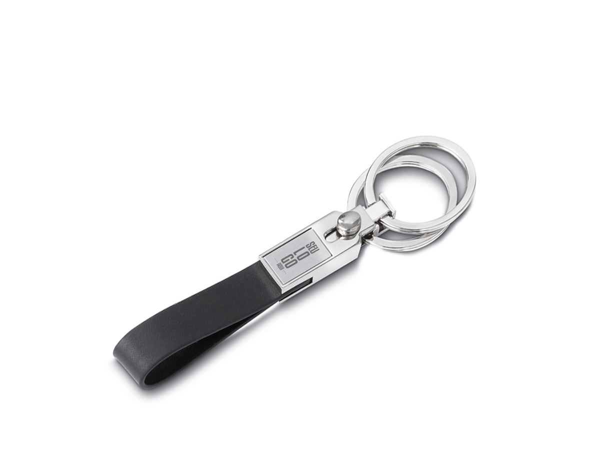 Chaveiro metal com duas argolas e alça em couro sintético, área frontal com plaquinha escovada e verso com 6 parafusos. Possui “botão” que permite a remoção da argola superior do chaveiro.